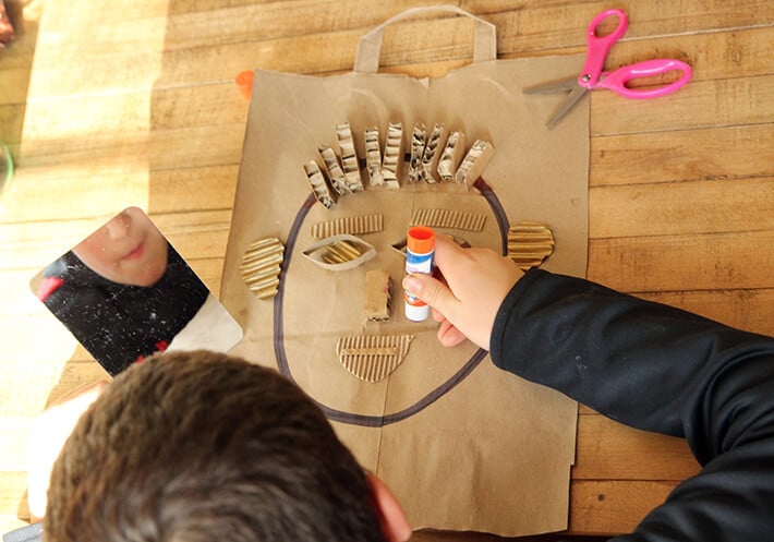 Child looking in mirror while creating self-portrait collage. 